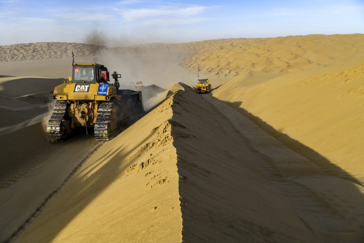 在新疆尉犁至且末沙漠公路施工现场，工人驾驶大型推土机推平沙山（5月16日摄）。