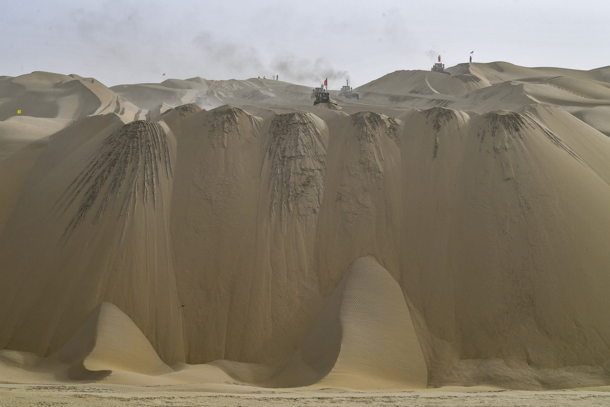 在新疆尉犁至且末沙漠公路施工现场，工人驾驶大型推土机推平沙山（5月17日摄）。