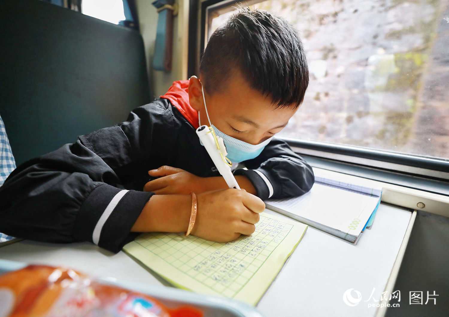 5633次列車上，一名彝族男孩正在寫作業。（李鍇 攝）