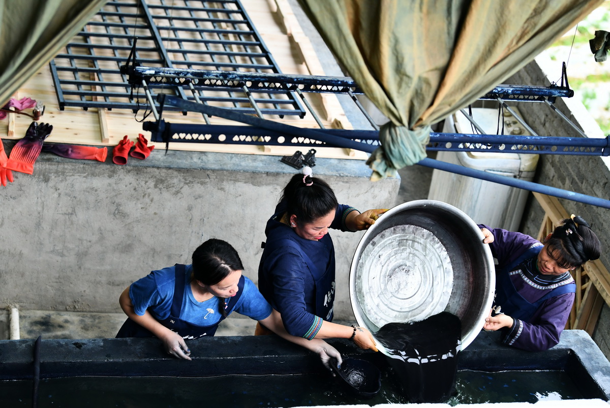杨成兰（左一）和村民一同把植物制作的染料倒入染缸（5月28日摄）。