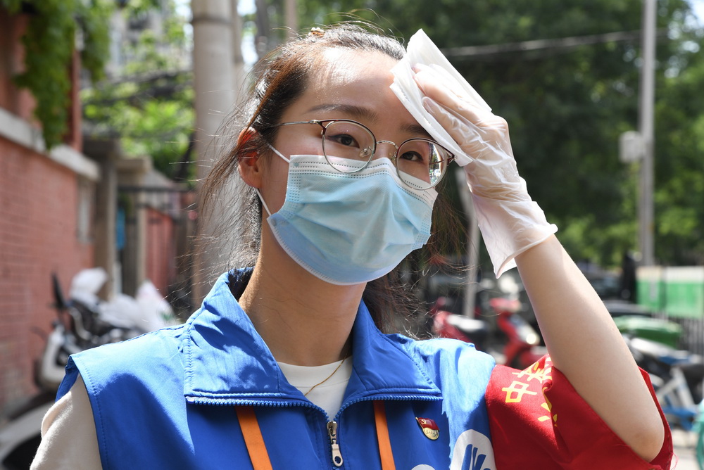 6月16日，在北京市海澱區中關村街道白塔庵社區出入口，疫情防控志願者王玥在擦拭汗水。