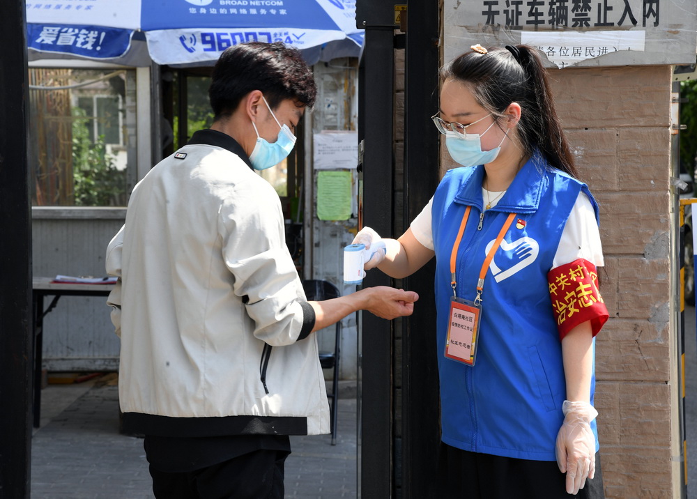 6月16日，在北京市海澱區中關村街道白塔庵社區出入口，疫情防控志願者王玥（右）測量社區居民的體溫。