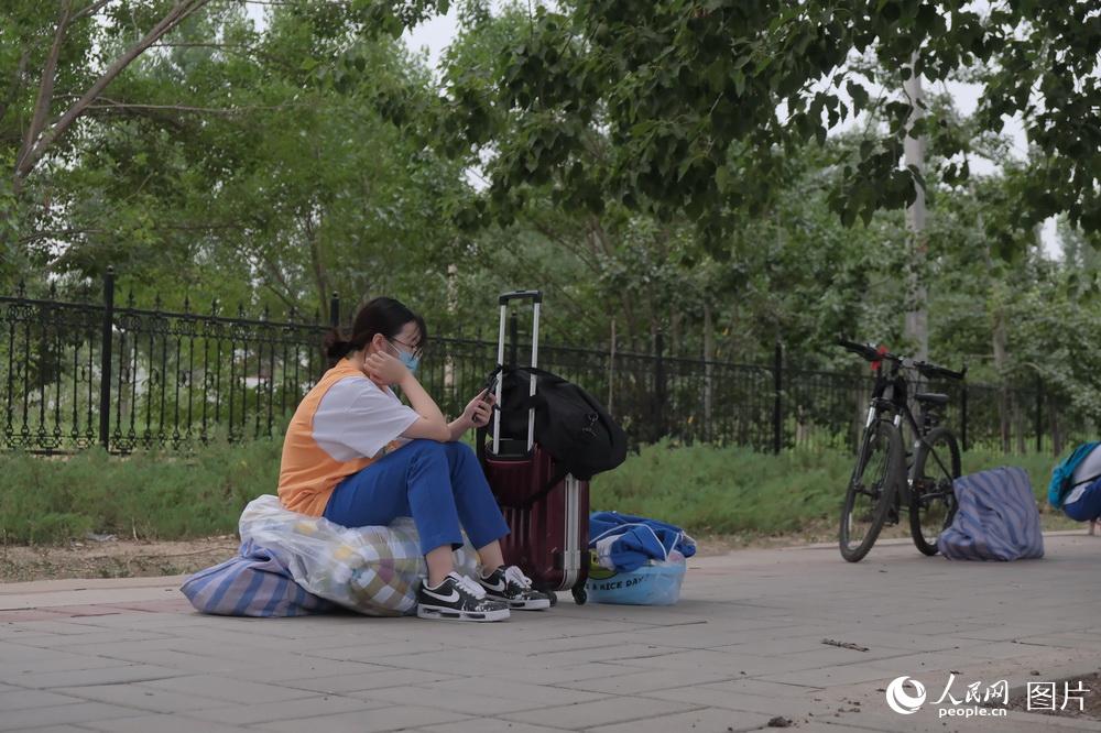 一名女生坐在整理好的行李上等待家長。（6月17日）人民網 張若涵 攝