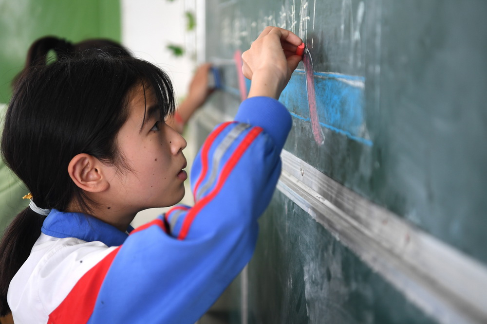 6月19日，在金寨縣三合實驗學校，蔡齊艷和同學一起做黑板報。