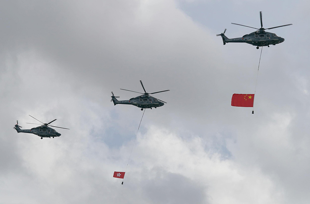 圖為直升機懸挂國旗和區旗飛過維港上空。