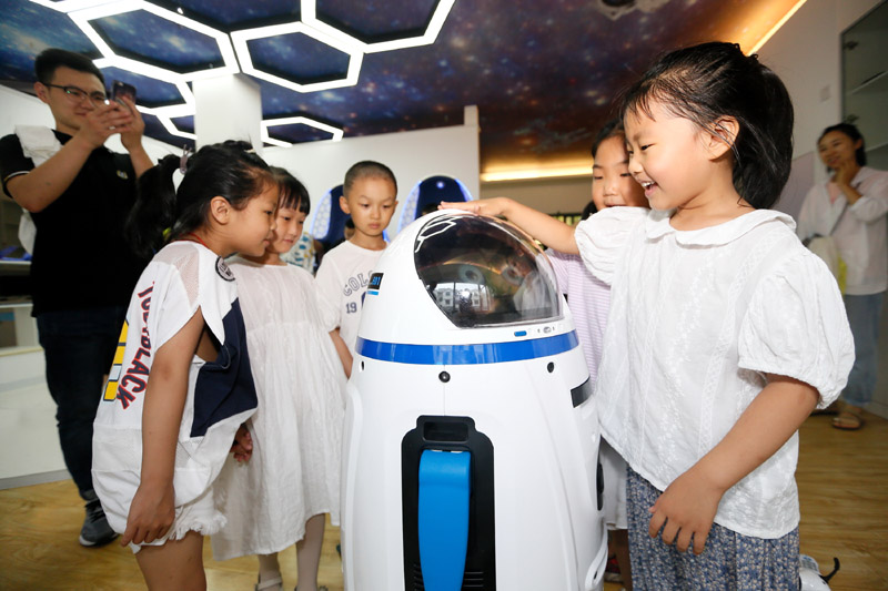 7月12日，小學生在山東省青島市即墨區環秀街道濱湖社區科普館與機器人互動。