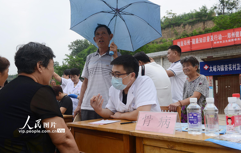 7月14日，鞏義市大峪溝鎮杏花村，村民在給義診的鄭州市骨科醫院的醫生打傘遮擋陣雨。