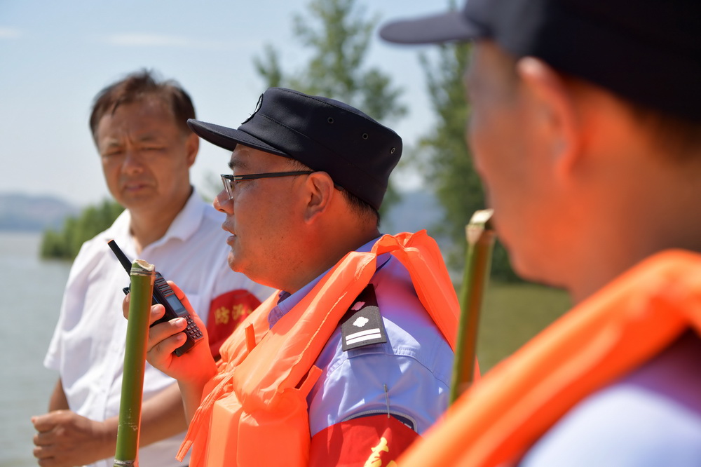 7月22日，梅玉勝（中）和同事們在防洪堤壩上巡邏，他通過對講機和其他小組的同事溝通。