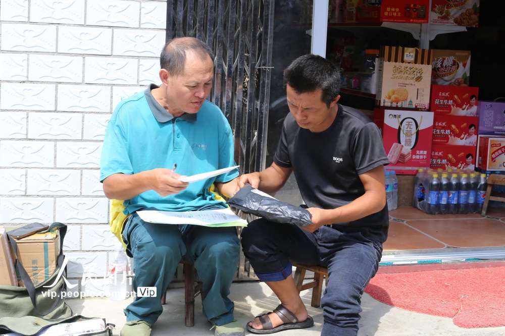 7月29日，在貴州省錦屏縣河口鄉韶靄村，張林昌（左）把郵件交到村民的手裡。