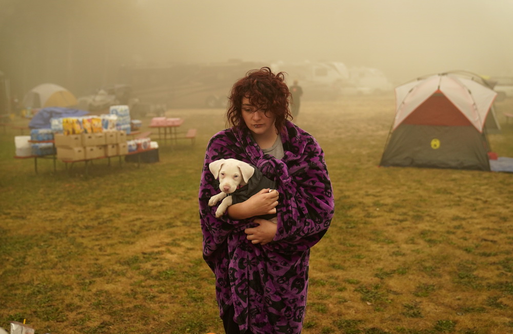 9月13日，在美国俄勒冈州奥克格罗夫，受灾居民抱着一只小狗站在避难中心的帐篷外。新华社/美联