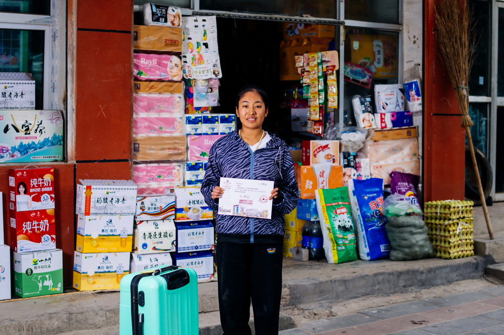 9月16日，在青海省化隆回族自治县巴燕镇，娘毛吉在乡间班车停靠点边的小卖部前展示自己的大学录取通知书。