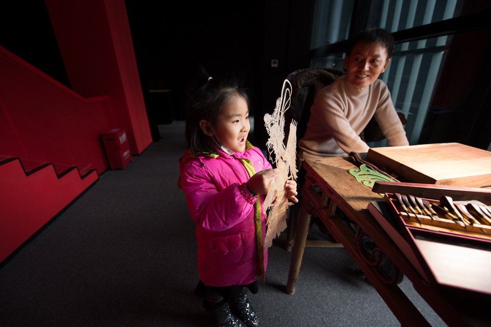 1月7日，在陕西西安明清皮影艺术博物馆，一名前来参观的小女孩拿起一幅先前雕刻好的皮影骨架。