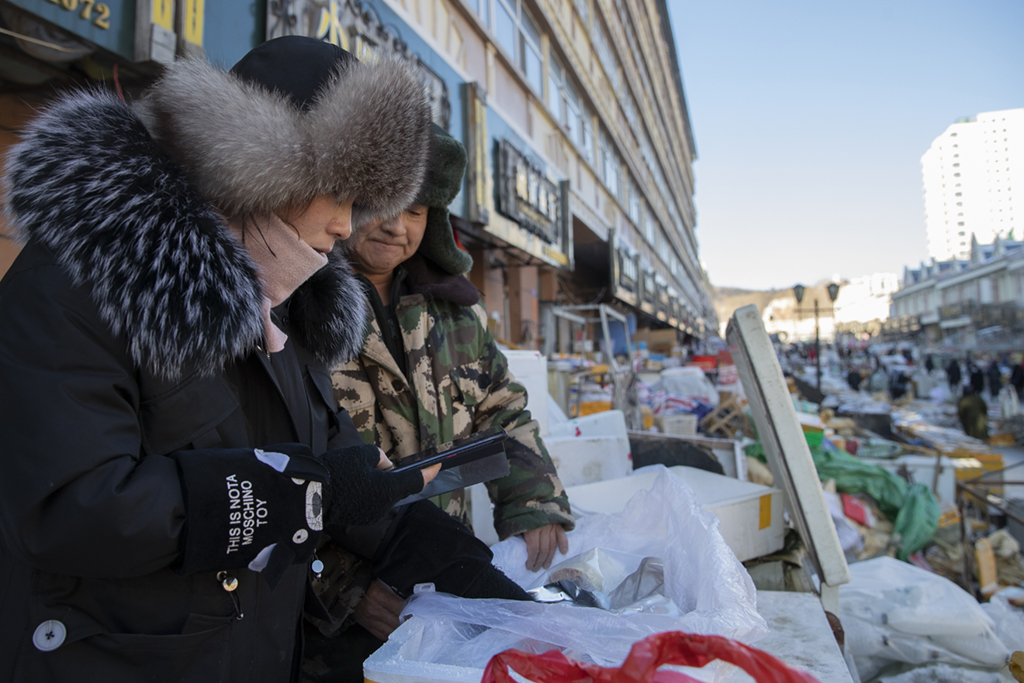 1月9日，商戶在撫遠“東極魚市”內用手機視頻的方式幫助顧客查驗魚產品。