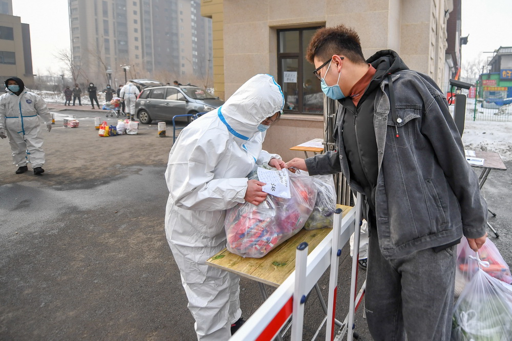 1月25日，王撼東（右）將幫居民採購的物品交給防疫工作人員。新華社記者 張楠 攝