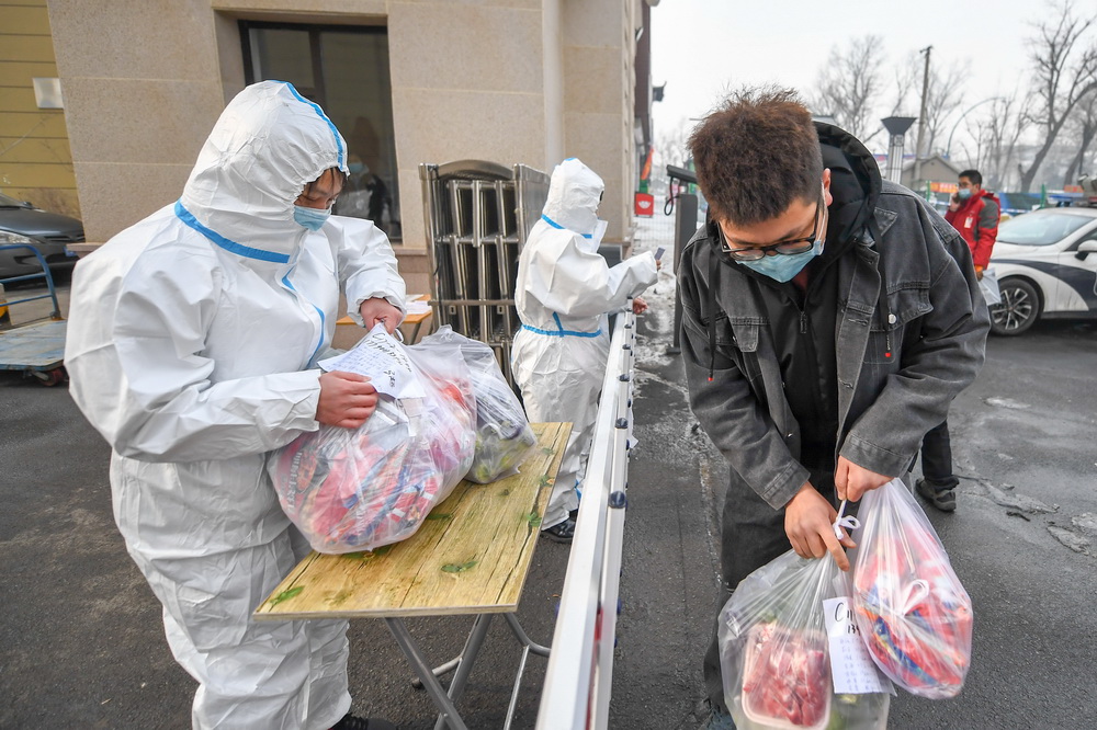 1月25日，王撼東（右）將幫居民採購的物品交給防疫工作人員。新華社記者 張楠 攝