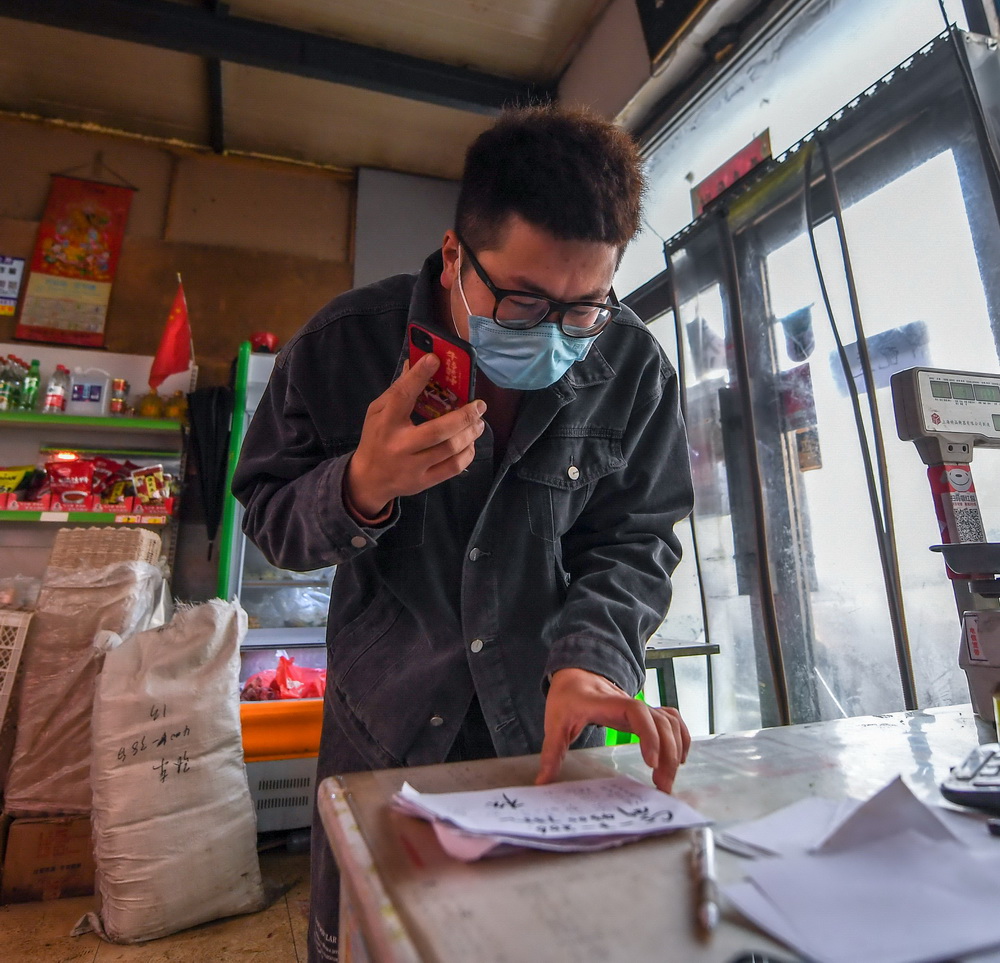 1月25日，王撼東在商店裡與封閉小區內的居民核對買菜清單。新華社記者 顏麟蘊 攝