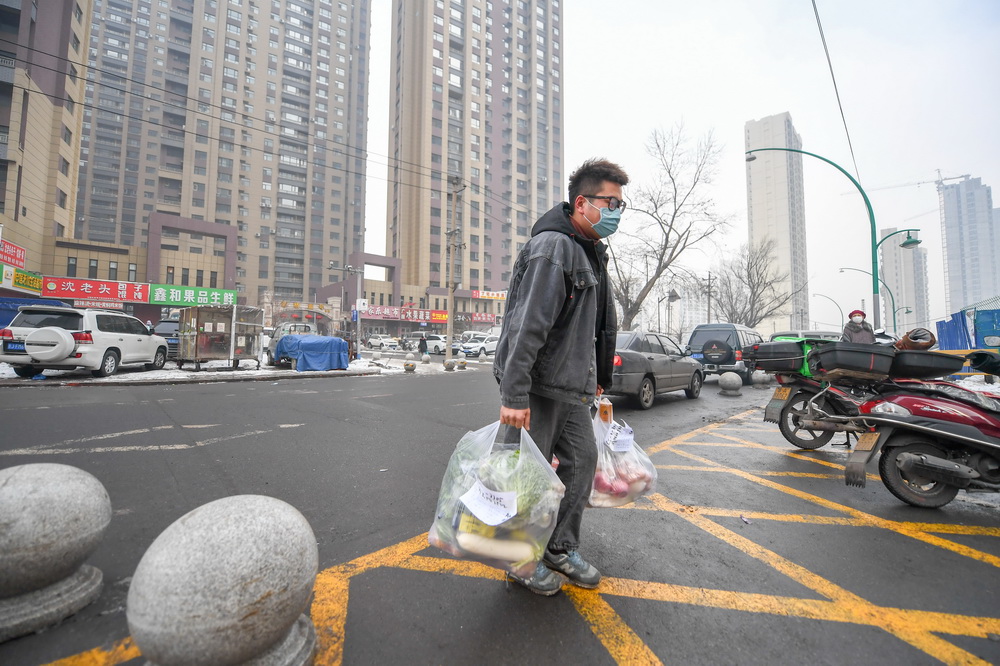 1月25日，王撼東拎著幫居民採購的物品走向封閉小區門口。新華社記者 張楠 攝