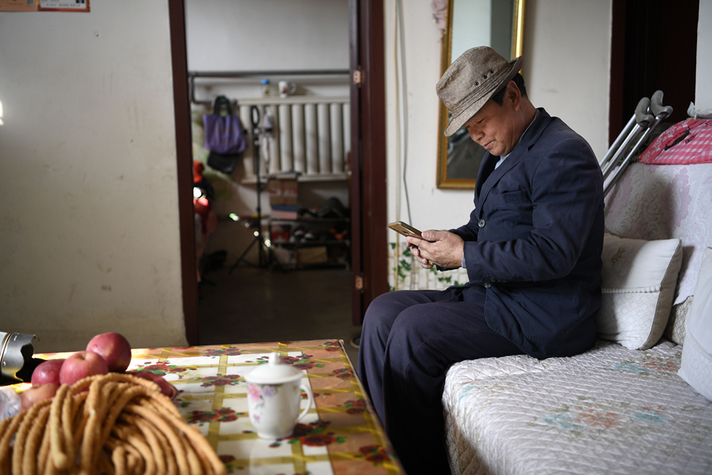 2月11日，張俊明在濱河家園移民村的家中翻看手機，准備網購一些家庭用品。新華社記者 王鵬 攝