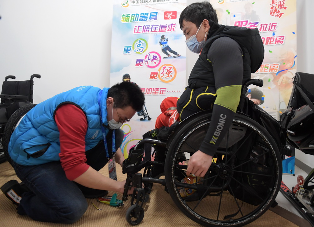 2月23日，延庆赛区国家高山滑雪中心的工作人员（左）正在为残疾人运动员调整轮椅。