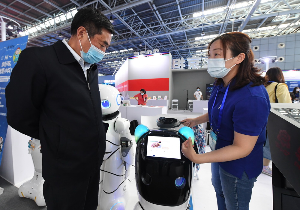 5月24日，在北京科技周活动主场室内主题展区，工作人员（右）为观众介绍家用功能型机器人。