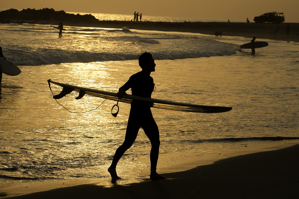 6月16日，一名沖浪者走在美國西部加利福尼亞州洛杉磯的一處海灘上。新華社/美聯
