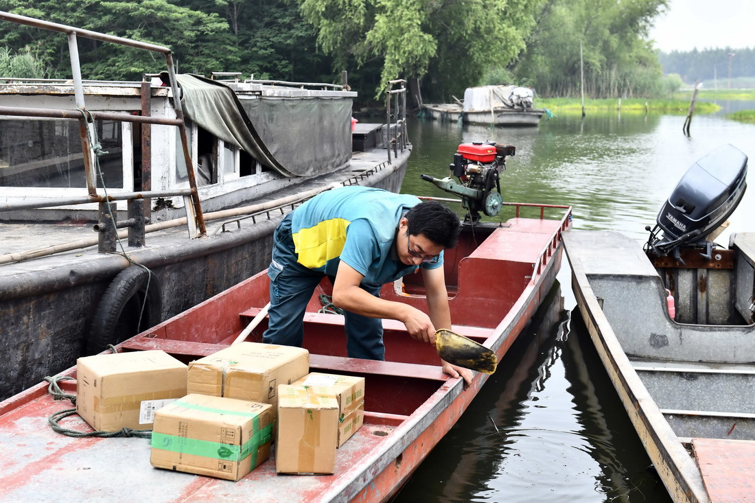 6月20日，在微山縣南陽鎮，郵遞員王少朋在清理郵船上的積水。