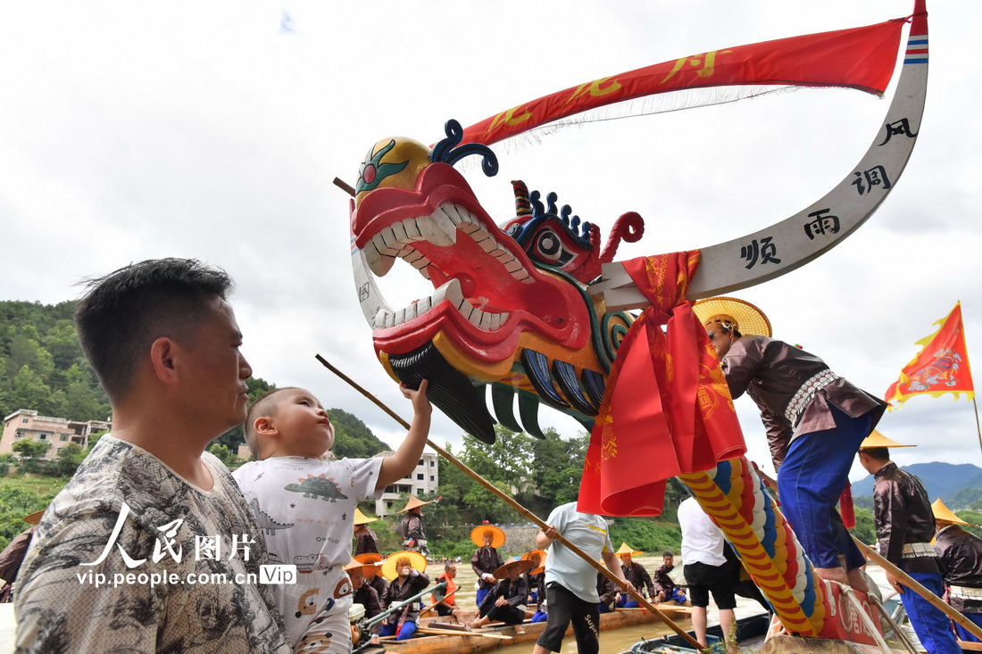 7月4日，貴州省台江縣施洞鎮清水江，一苗族村民抱著小孩去觸摸獨木龍舟的龍頭祈福。