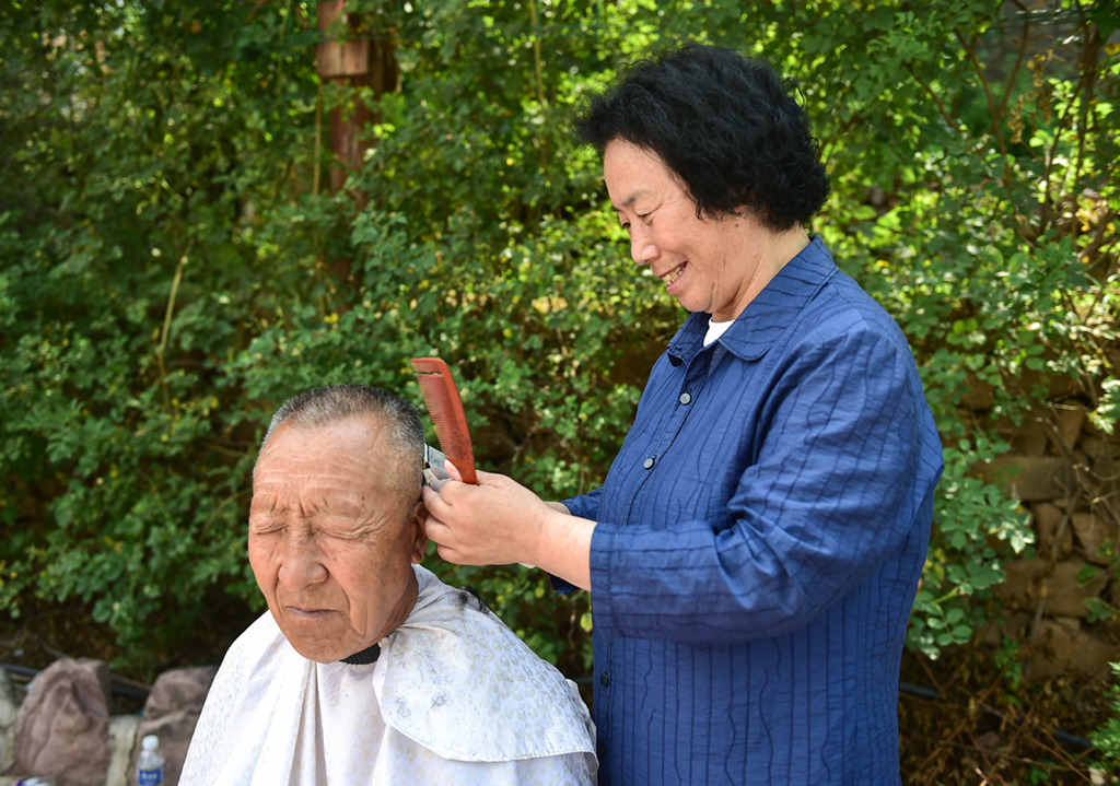 7月7日，在山西省阳城县东哄哄村，栗红连（右）给村里的老人理发。