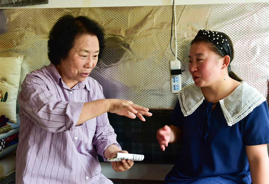 7月6日，在山西省阳城县东关村的红连理发店，栗红连（左）用自制的小卡片教聋哑徒弟贾一凡发音。