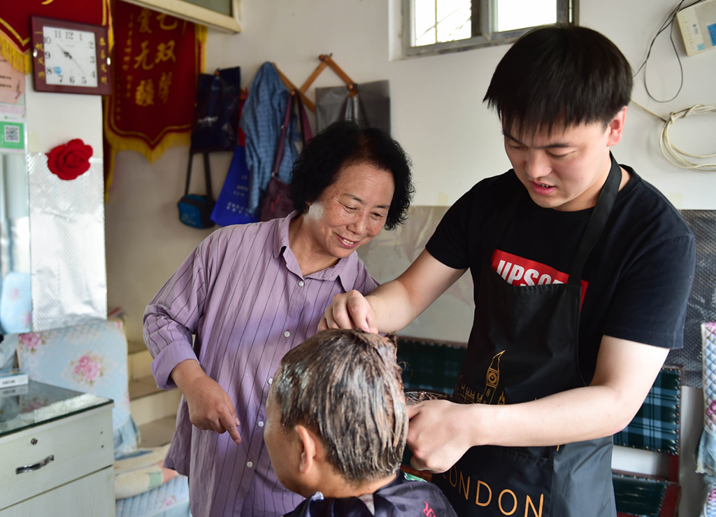7月6日，在山西省阳城县东关村的红连理发店，栗红连（左）教徒弟崔浩男染发技巧。