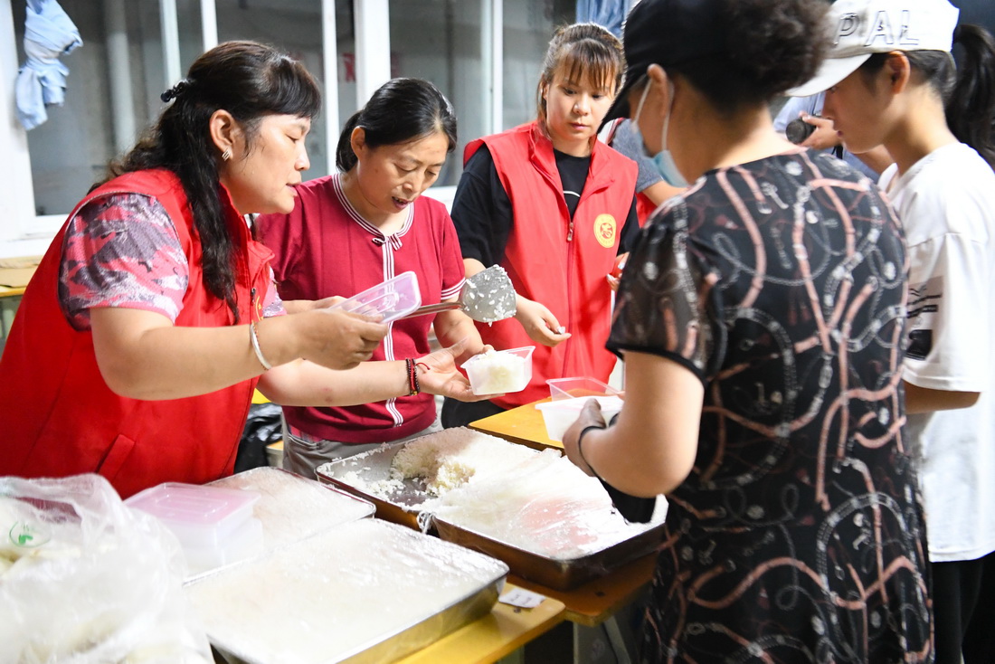 7月21日，在鄭州市電子信息工程學校集中安置點，志願者為轉移群眾發放晚餐。