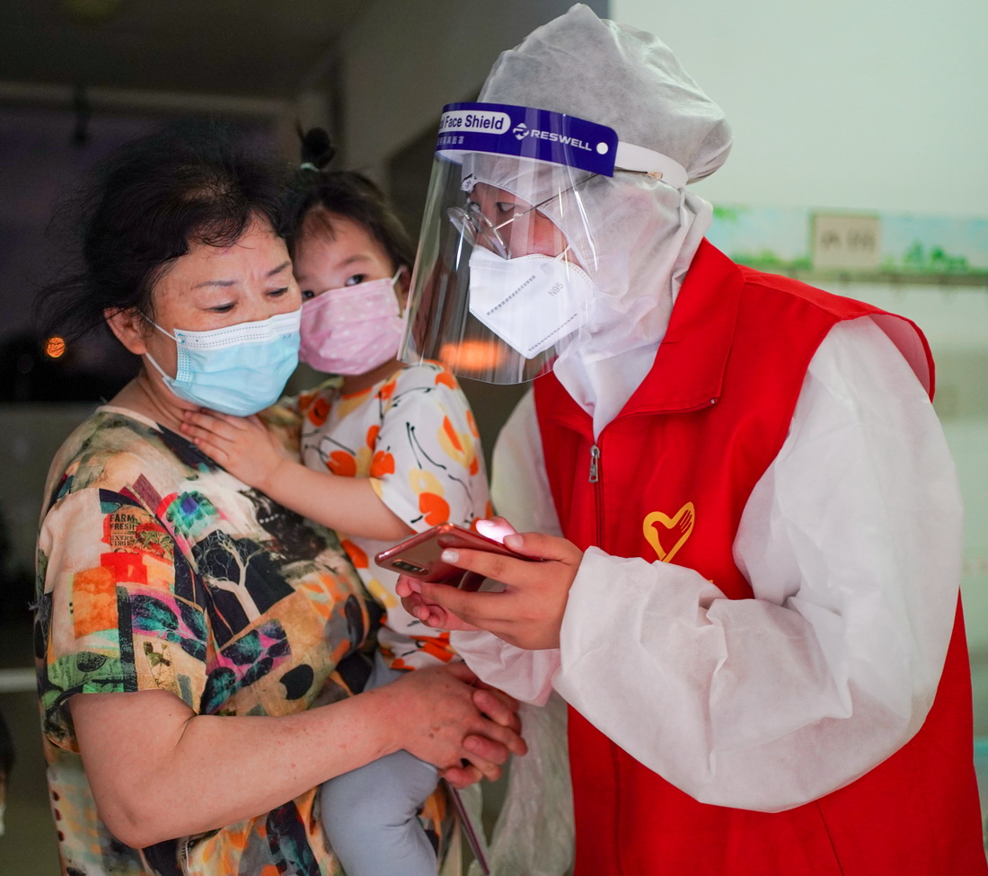 7月24日，在南京市江寧區龍西社區核酸檢測點，志願者程玉潔（右）幫助前來做核酸檢測的居民進行微信小程序預約。新華社記者 李博 攝