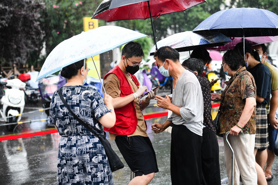 7月25日，在南京市鼓樓區五台山體育中心，志願者花宇鑫（左二）工作時被大雨淋濕，居民為其撐傘。新華社記者 季春鵬 攝