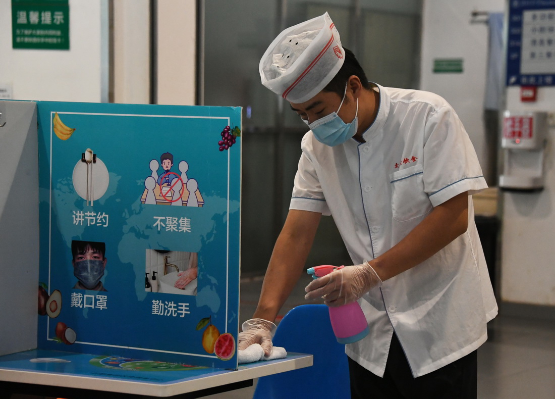 8月9日，在北京交通大学学生第二食堂，工作人员对餐桌进行消毒。