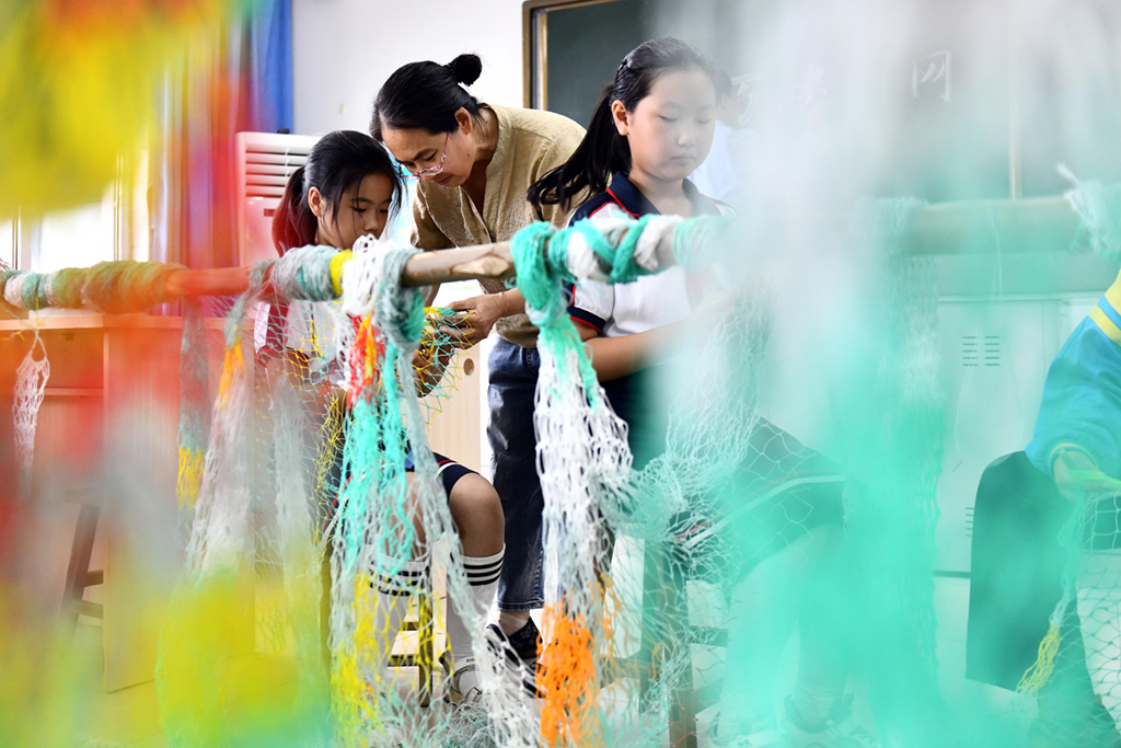 9月3日，在日照市岚山区岚山头小学，老师在指导学生学习织渔网。