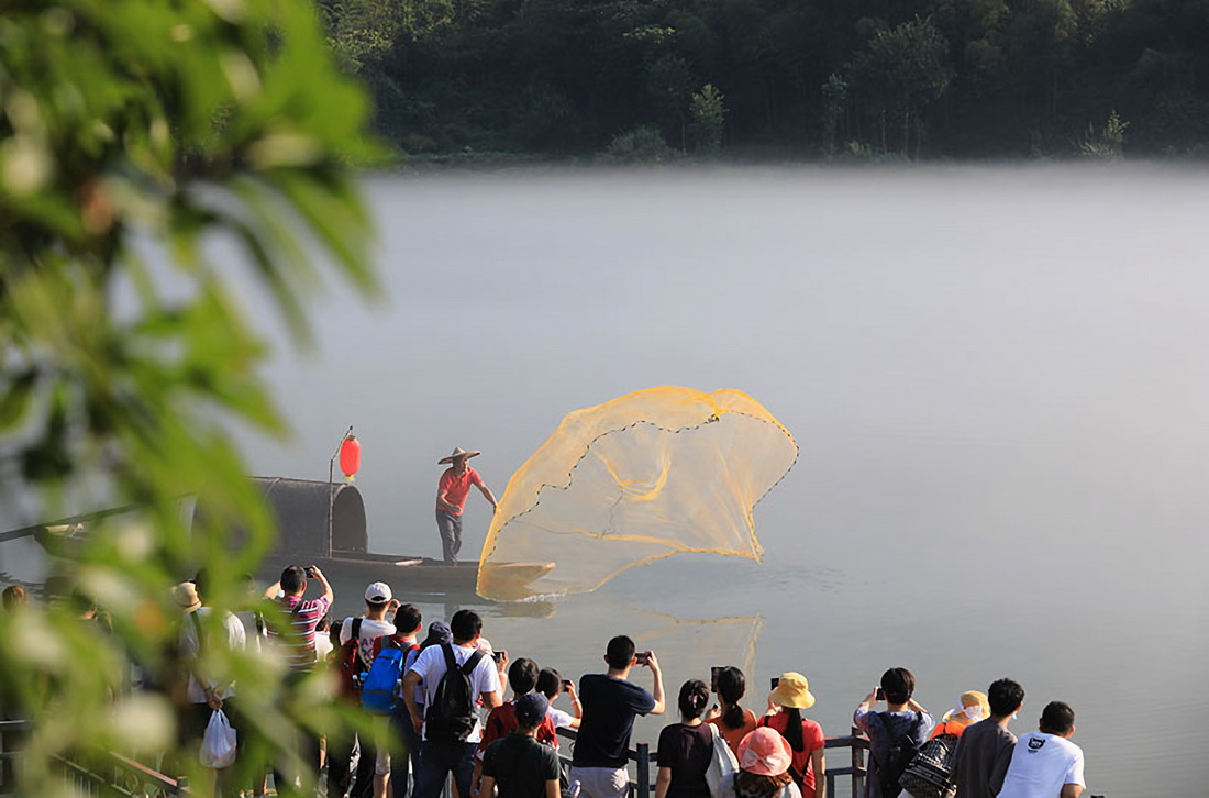 10月5日，游客在湖南省资兴市东江湖旅游区欣赏渔夫撒网表演。新华社发（朱孝荣 摄）