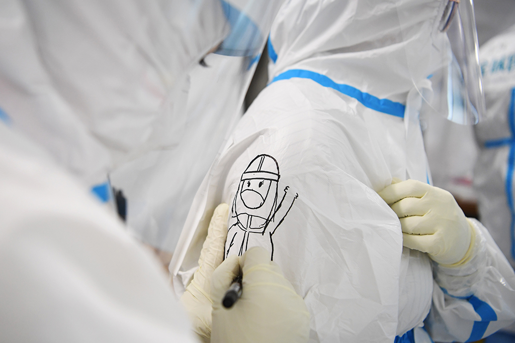 10月24日，“獵鷹號”硬氣膜實驗室工作人員普臣惠（左）給同伴的防護服上畫上卡通圖案，為同伴加油鼓勁。