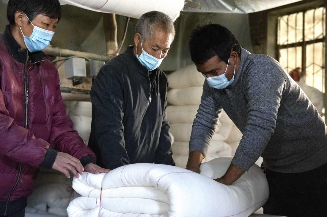 在新疆沙雅縣蓋孜庫木鄉的一處棉花加工作坊裡，艾買爾·艾則孜（右）用手按壓剛做好的棉被，這是他用今年新採的自家棉花做的（10月26日攝）。