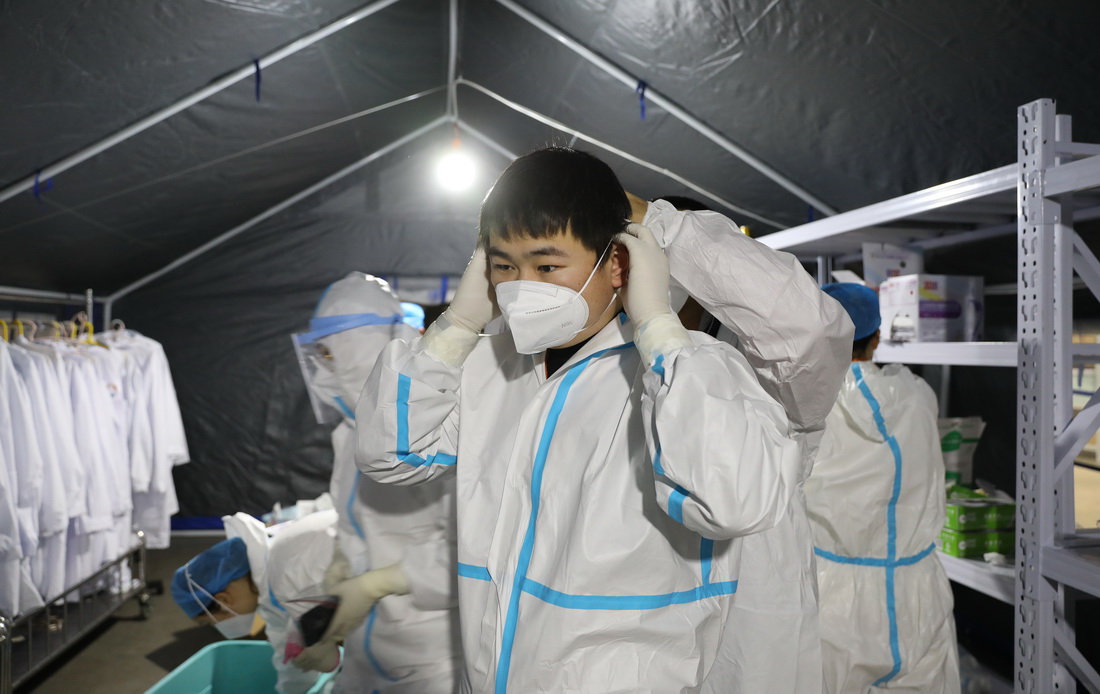 11月15日，大连方舱核酸检测实验室工作人员在更衣室内穿戴防护装备准备进入实验室。