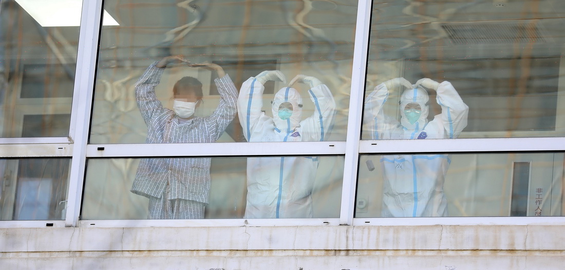 11月19日，兩名遼寧省新冠肺炎集中救治大連中心醫護人員和一名患者在隔離病房的走廊裡向窗外做出愛心手勢。新華社記者 姚劍鋒 攝