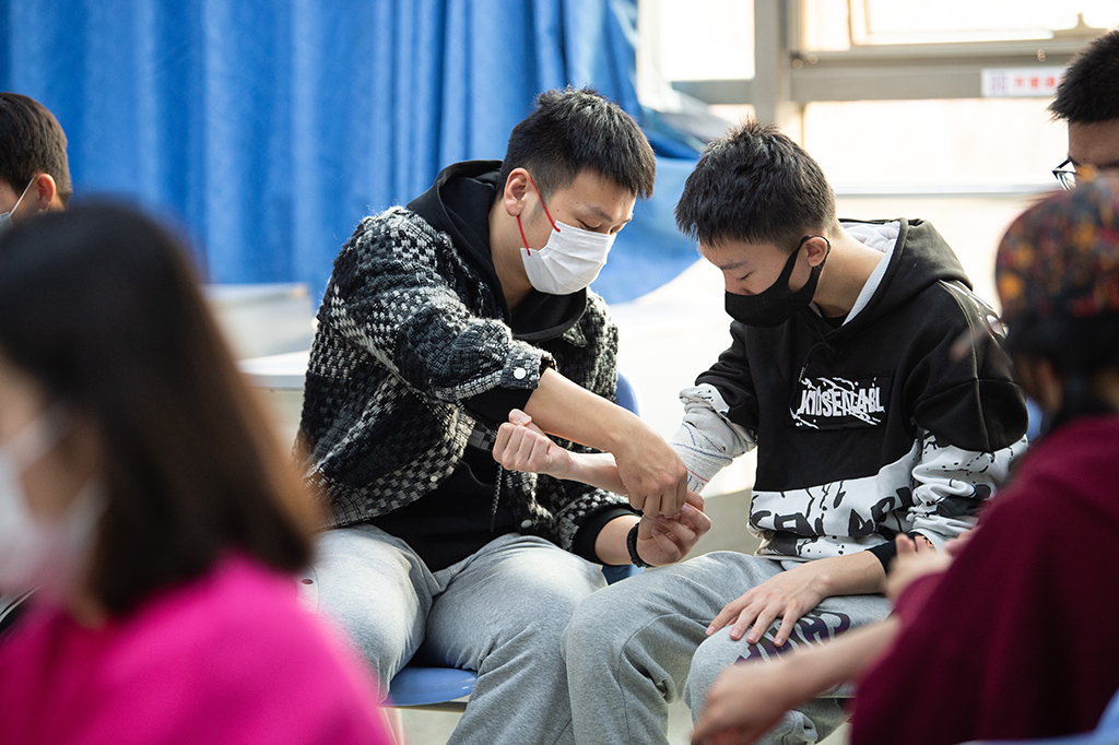 楊曦（右）在學校參加冬奧志願者急救技能培訓時與同學一起練習包扎（11月27日攝）。新華社記者 陳鐘昊 攝