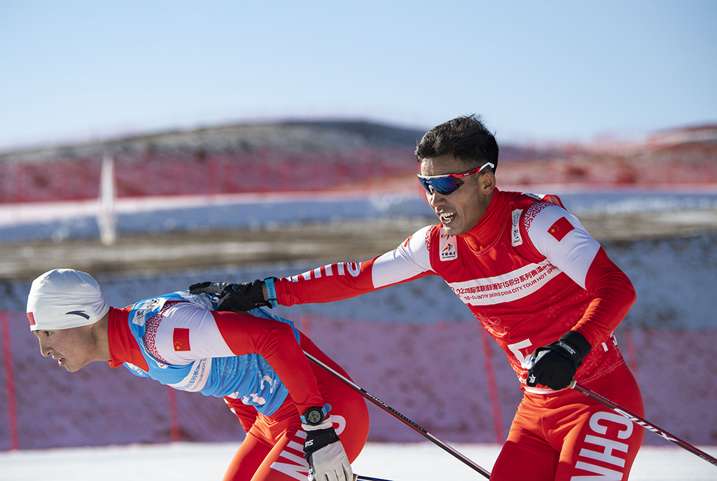 這是在2021-2022國際雪聯越野滑雪積分系列賽溫泉站男子團體短距離（傳統技術）的比賽中，吐爾鬆江·布爾力克（右）與隊友趙磊完成接力（2021年11月24日攝）。