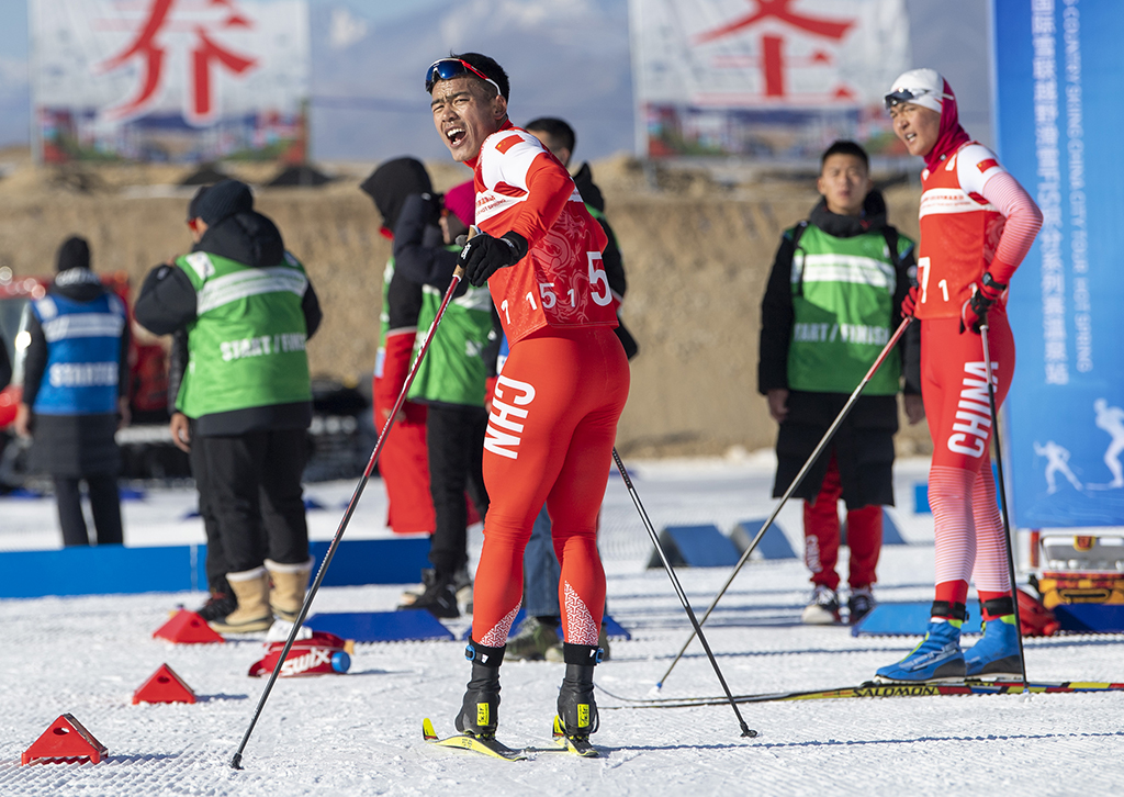 這是在2021-2022國際雪聯越野滑雪積分系列賽溫泉站男子團體短距離（傳統技術）的比賽中，吐爾鬆江·布爾力克在接力區等候隊友，並為他們吶喊加油（2021年11月24日攝）。