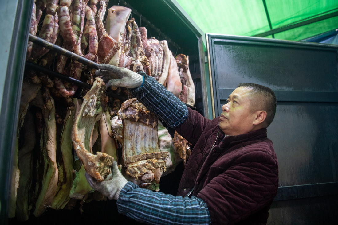 12月18日，在位於重慶市渝北區王家街道的“無煙熏制臘肉便民服務點”，工作人員將原材料放入“熏肉神器”。