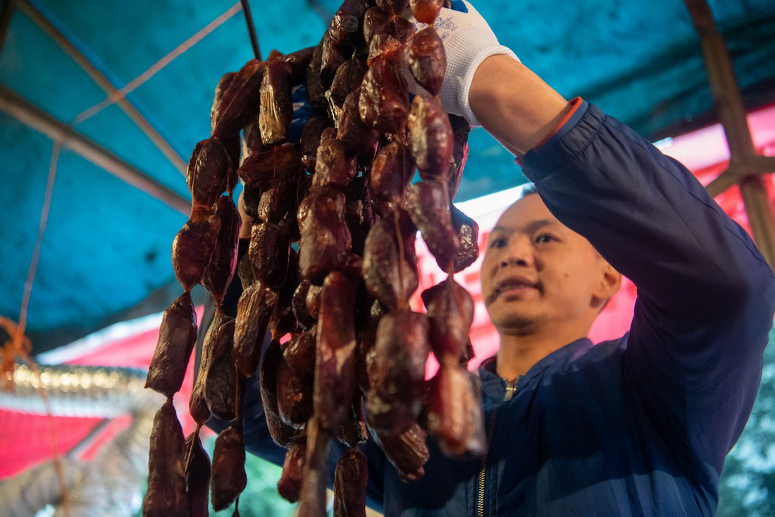 12月18日，在位於重慶市渝北區龍溪街道的“無煙熏制臘肉便民服務點”，工作人員在整理熏制好的臘味年貨。