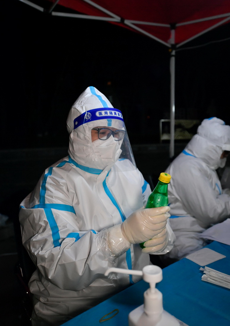 1月12日，在天津市南開區廣開街道某核酸檢測點，醫務人員在完成手部消毒后用灌有熱水的塑料瓶暖手。