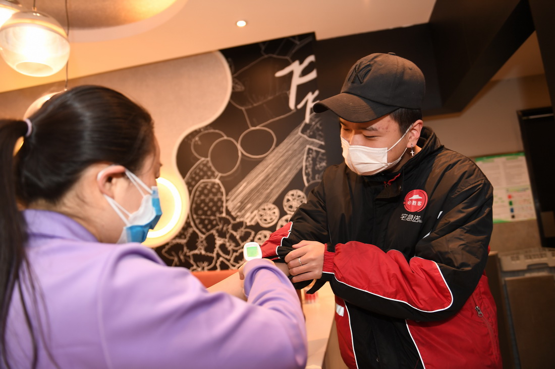 1月13日，在西安市一家連鎖餐廳，工作人員對配送員（右）測量體溫。