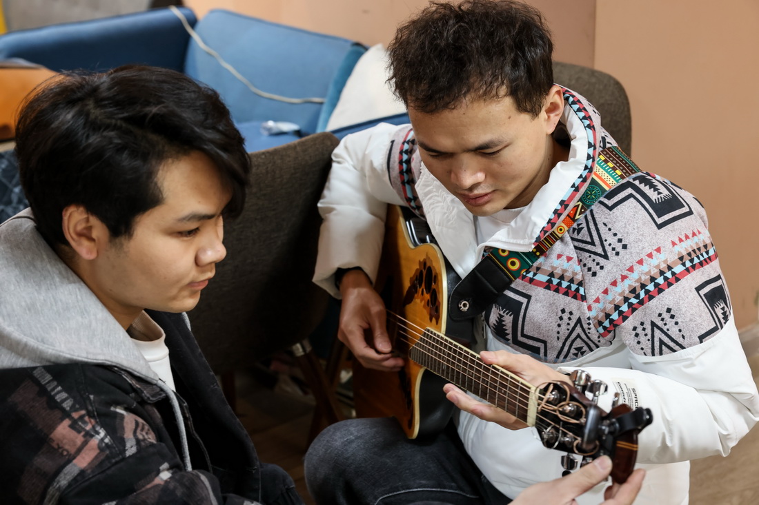 3月1日，“折耳根”樂隊貝斯手彭萬海（左）在幫助吉他手楊志調音。
