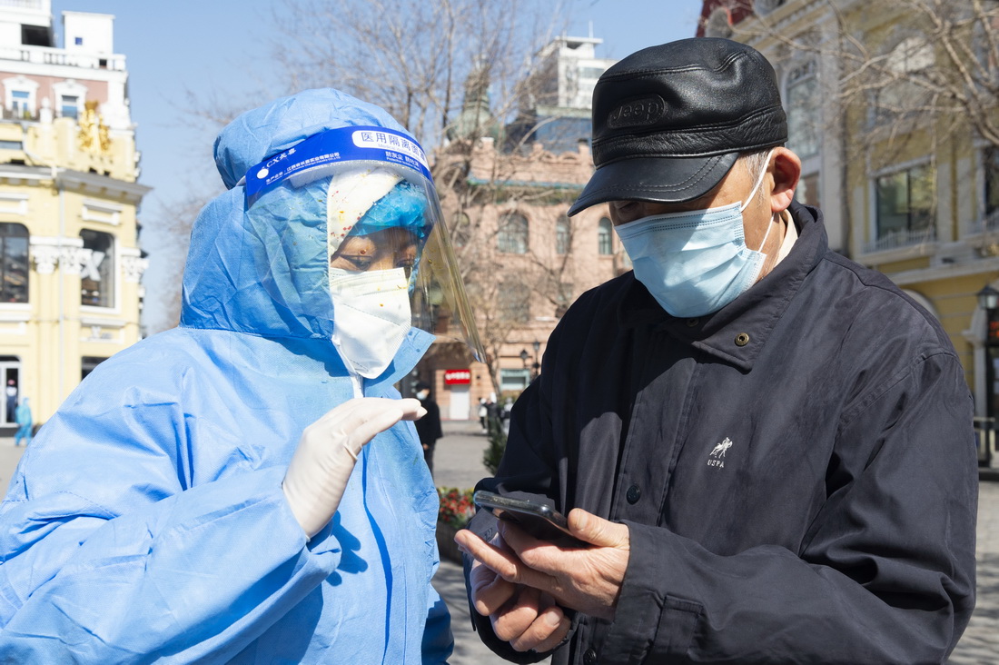 在哈尔滨市道里区一核酸采样点，街道工作人员（左）指导市民进行核酸采样（3月20日摄）。