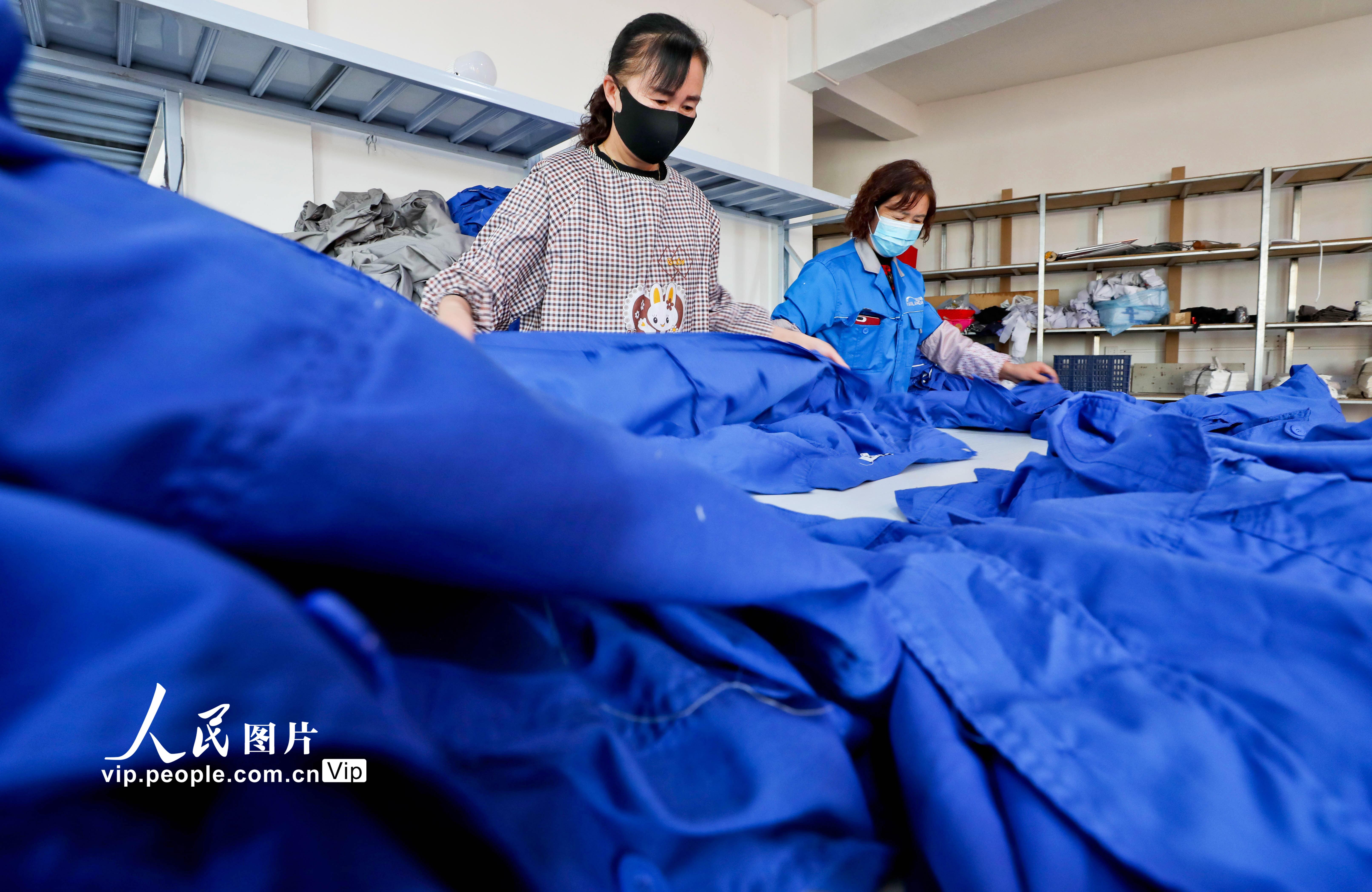 2022年3月24日，甘肅省張掖市山丹縣海蘭達服飾鄉村就業工廠內，女工們正在整理、熨燙加工好的工作服。